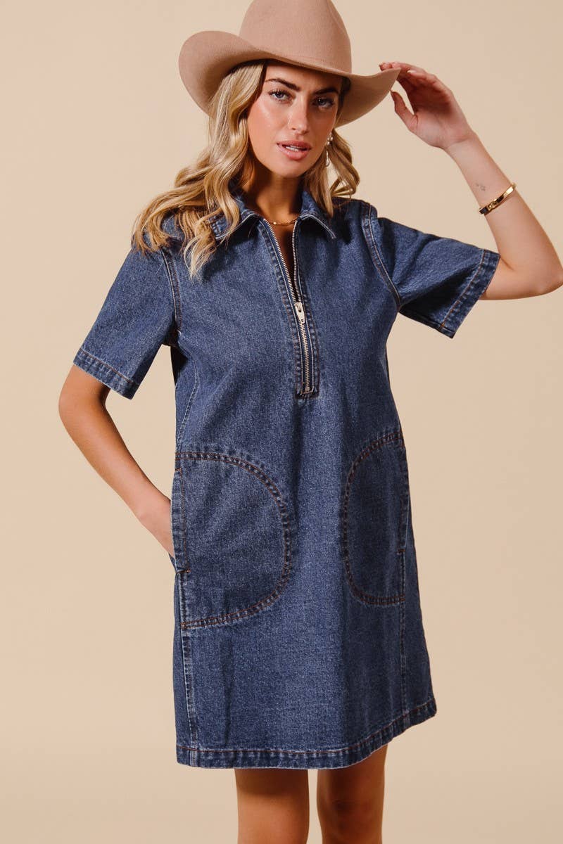 model wearing a denim dress with short sleeves, collar, front zipper and big front sewn pockets paired with a cowboy hat on a beige background