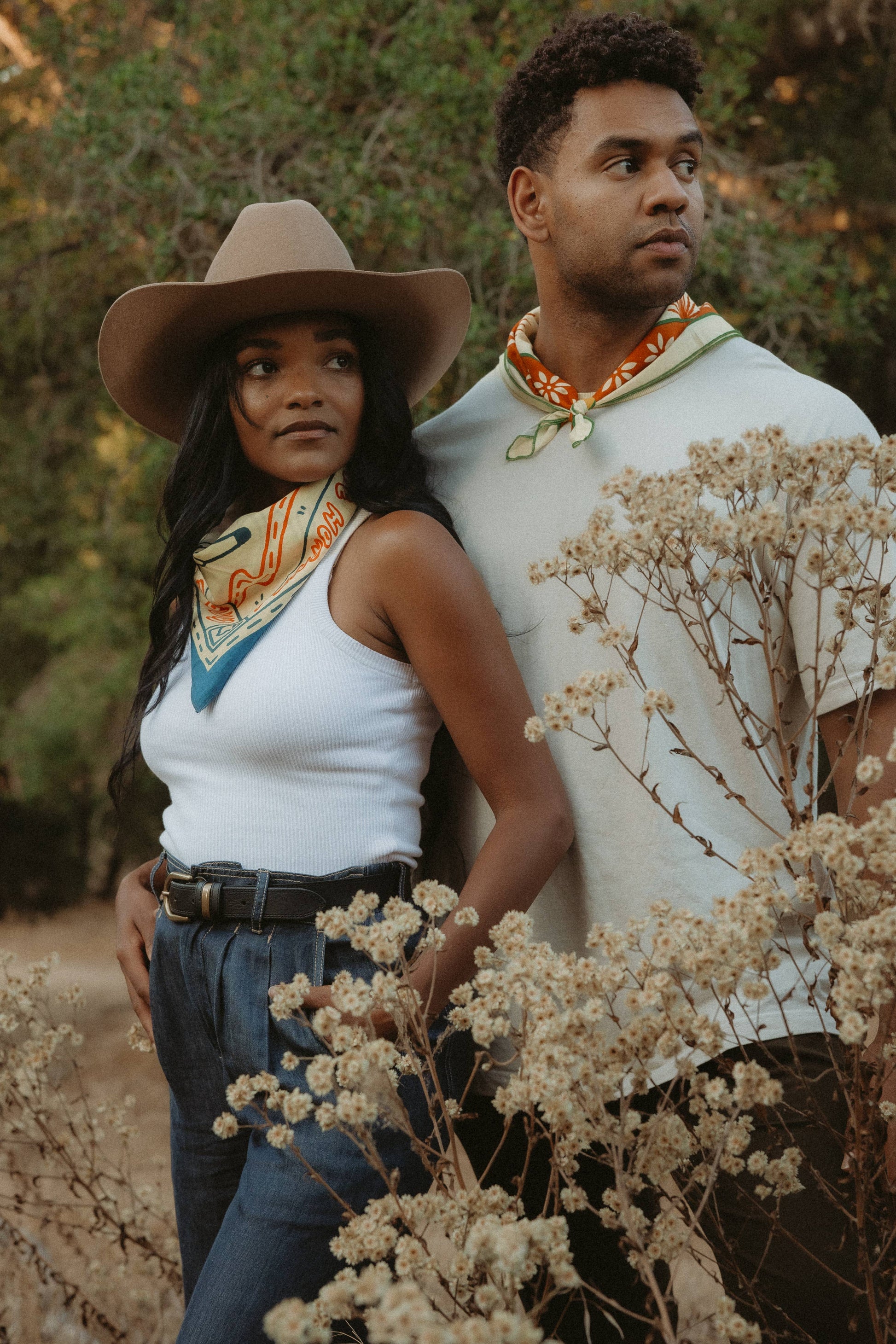 couple posed outside wearing white shirts, jeans and bandanas around necks