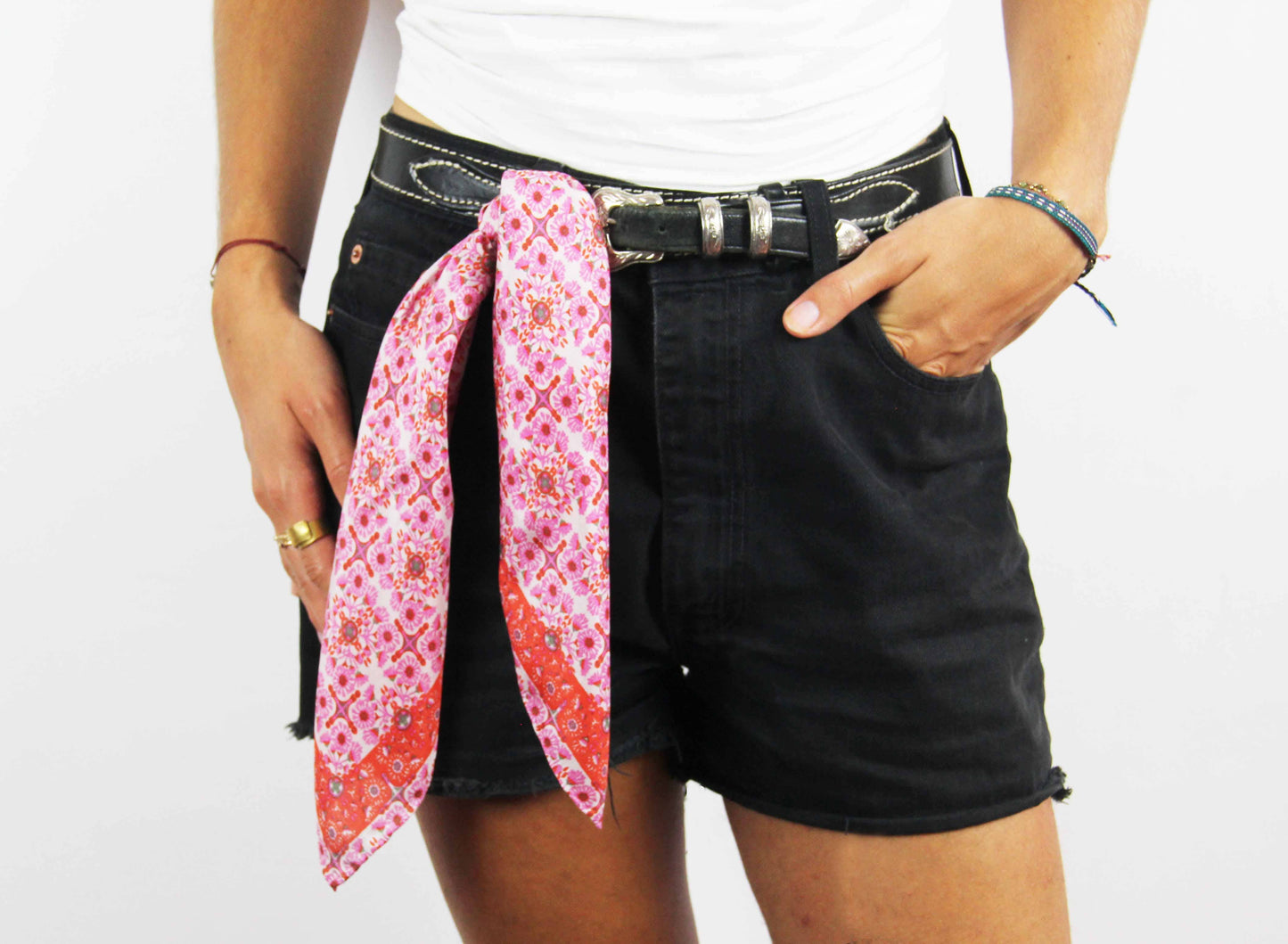 Person wearing black shorts with a pink and red patterned scarf over the waistband on a white background