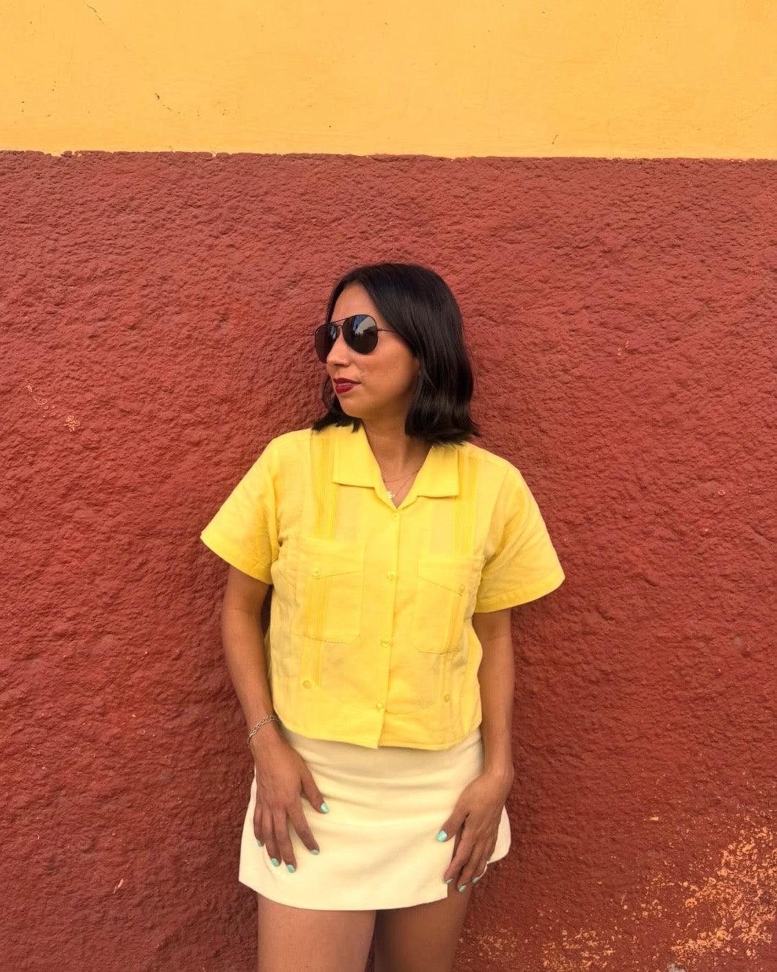 Woman wearing a yellow shirt and white skirt against a red and yellow wall.