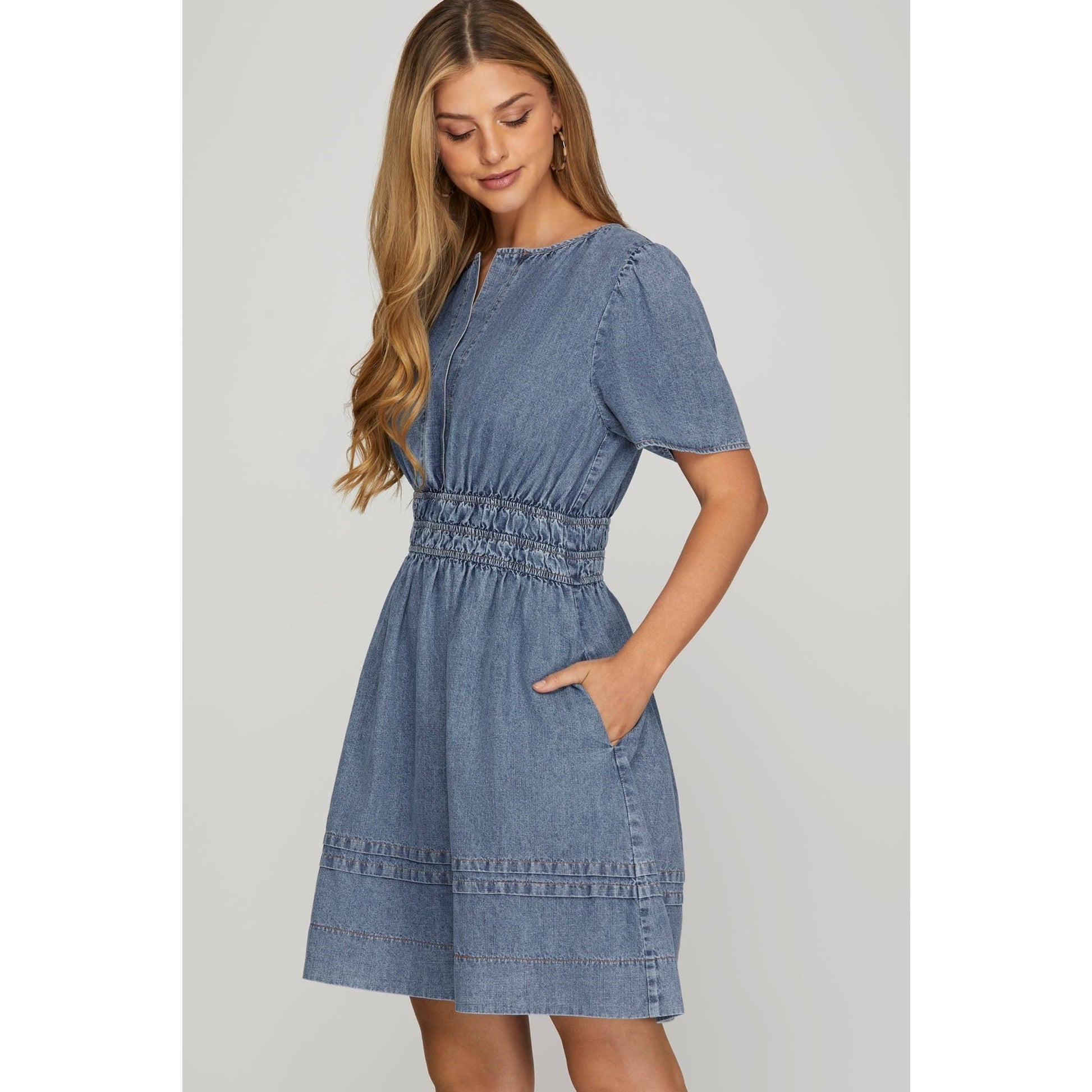 A woman wearing a blue washed denim short sleeve dress with elastic waistband and side pockets