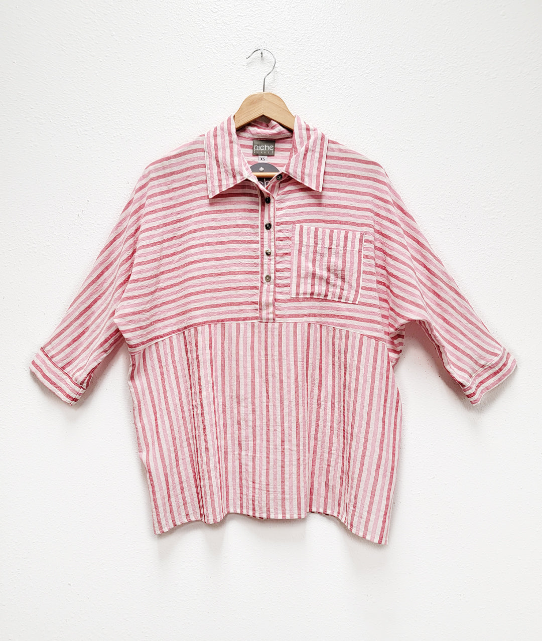 red and white striped top on a hanger. top has a placket down to natural waist and 3/4 sleeves