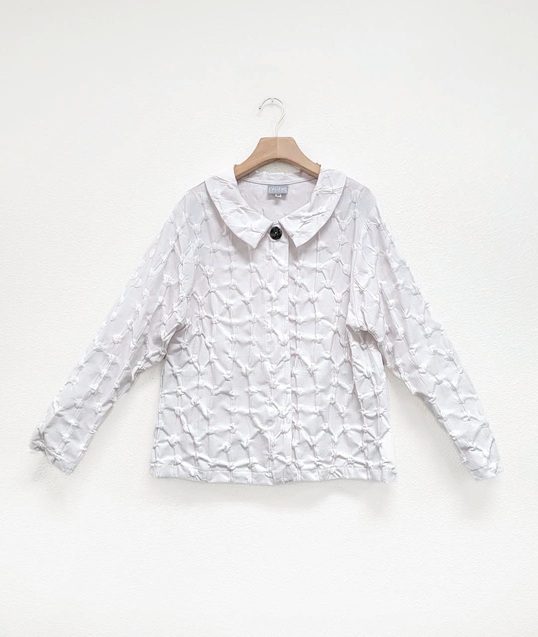 white blouse in a puckered dot texture. blouse has long sleeves, a collar, a hidden placket with snaps and a single large button at the top center