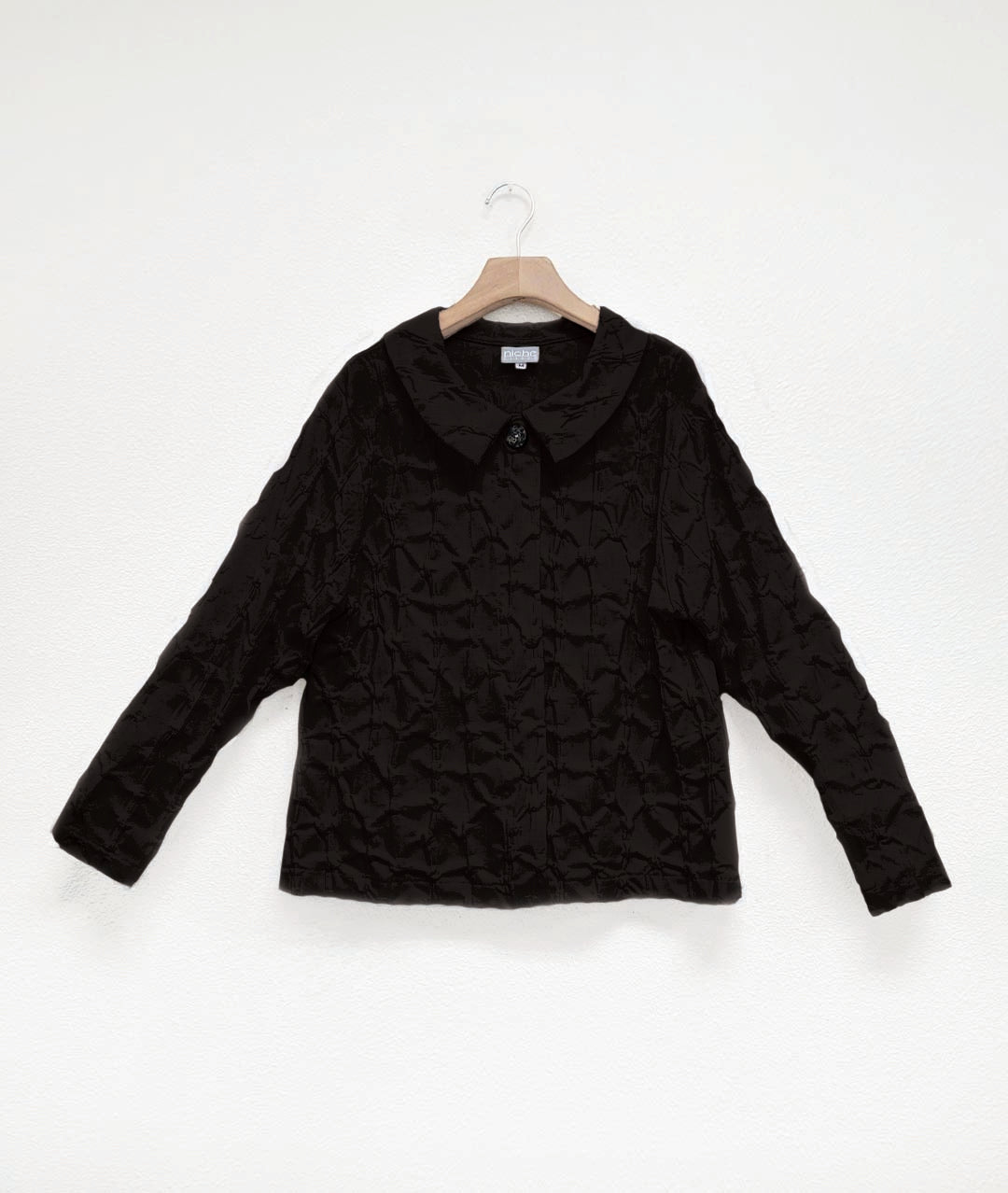 black textured blouse with a hidden placket with one decorative button at the neck. top has hip pockets and long sleeves