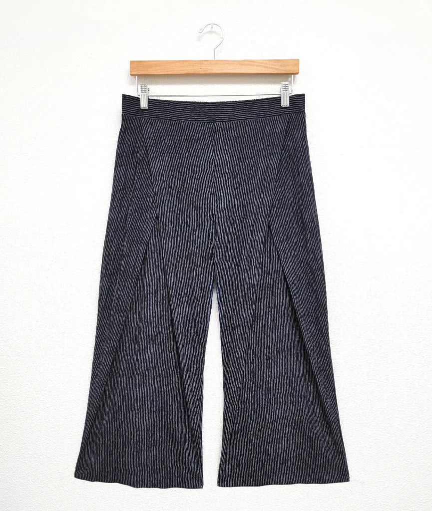 Grey pleated pants on a hanger against a white background