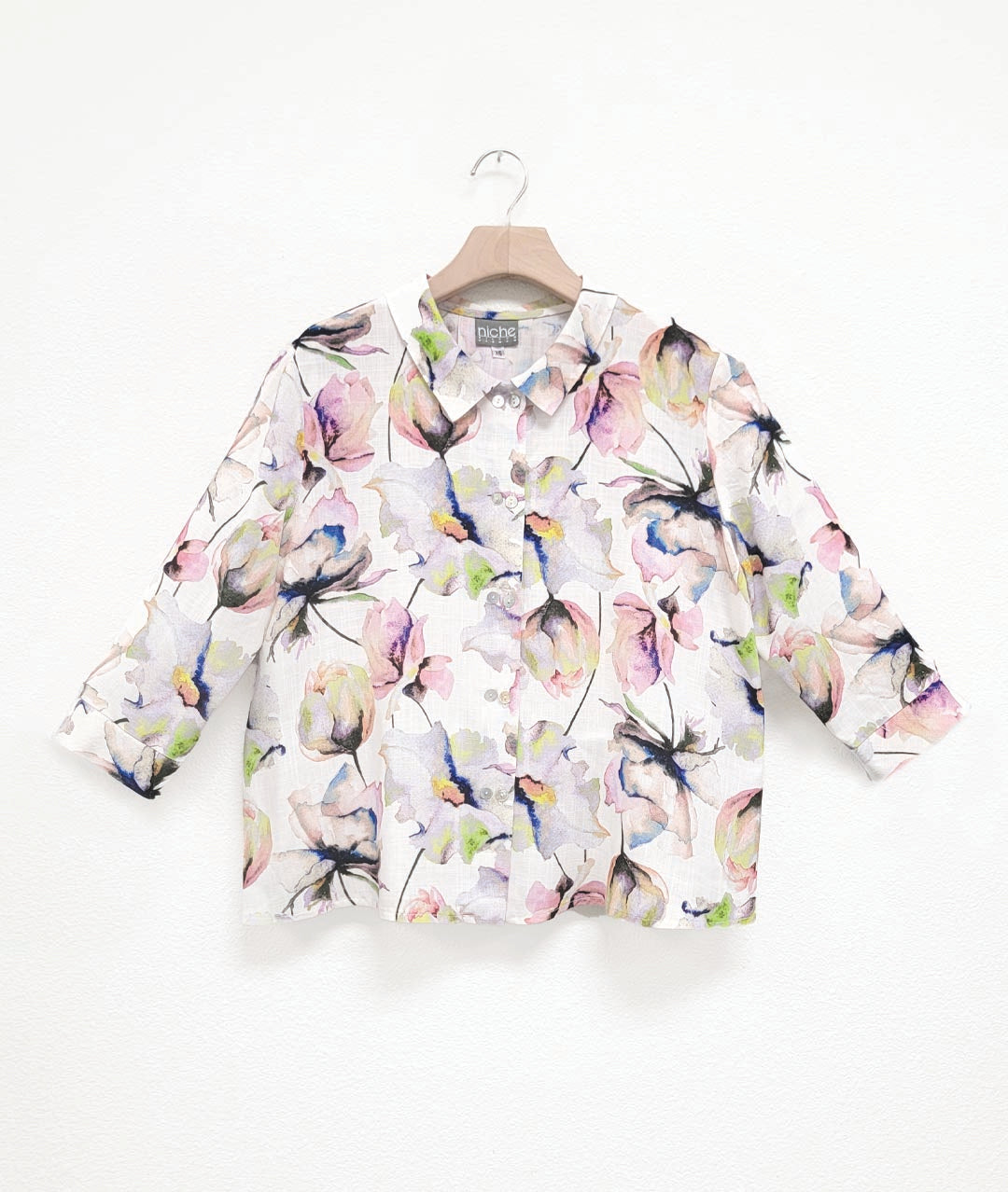 white button down blouse with a multicolor floral print. blouse has a cropped, boxy body, 3/4 sleeves and a twinbutton detail