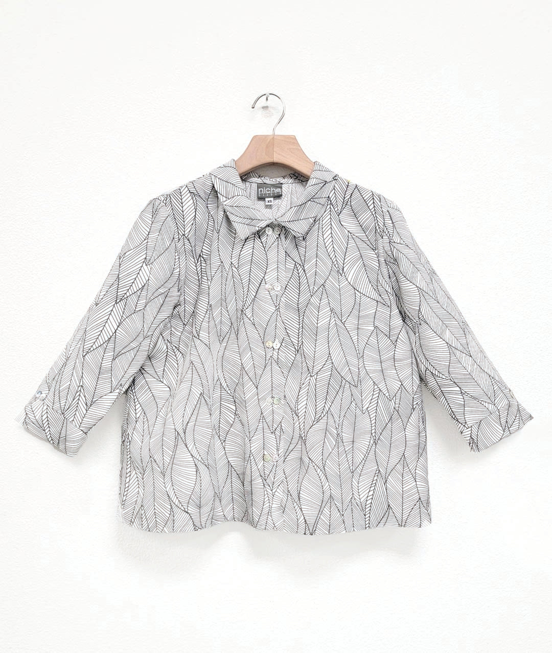 white button down blouse with a grey leaf print. blouse has a cropped, boxy body, 3/4 sleeves and a twinbutton detail