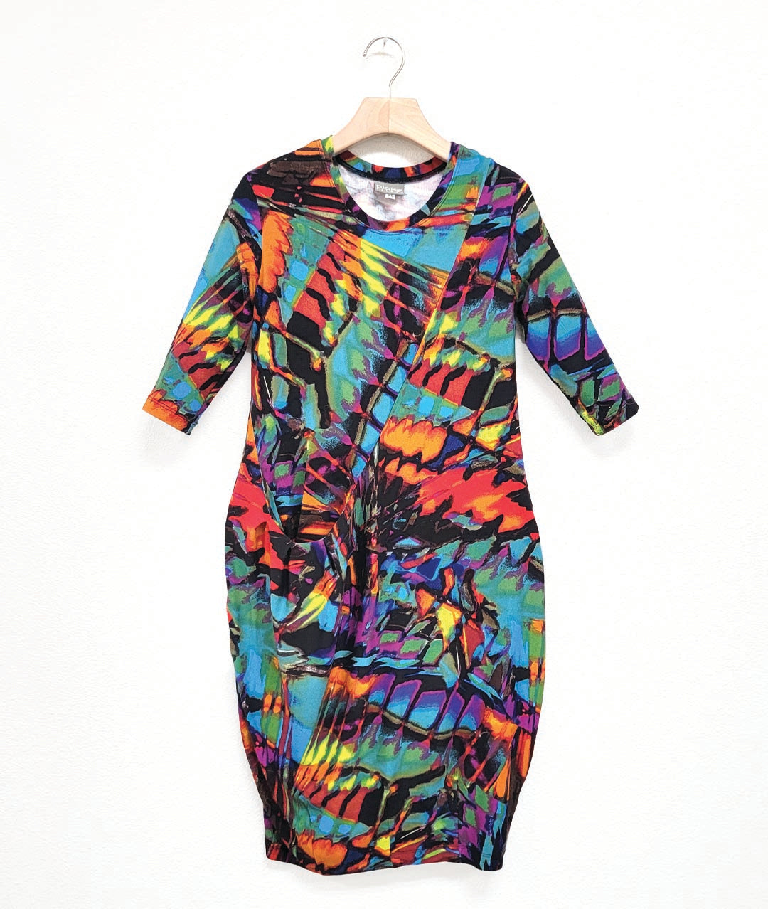 jersey dress with a round neckline, 3/4 sleeves, and an asymmetrical diagonal seam across the body, with a single hip pocket, highlighted by pleats. dress print is a multicolor mix