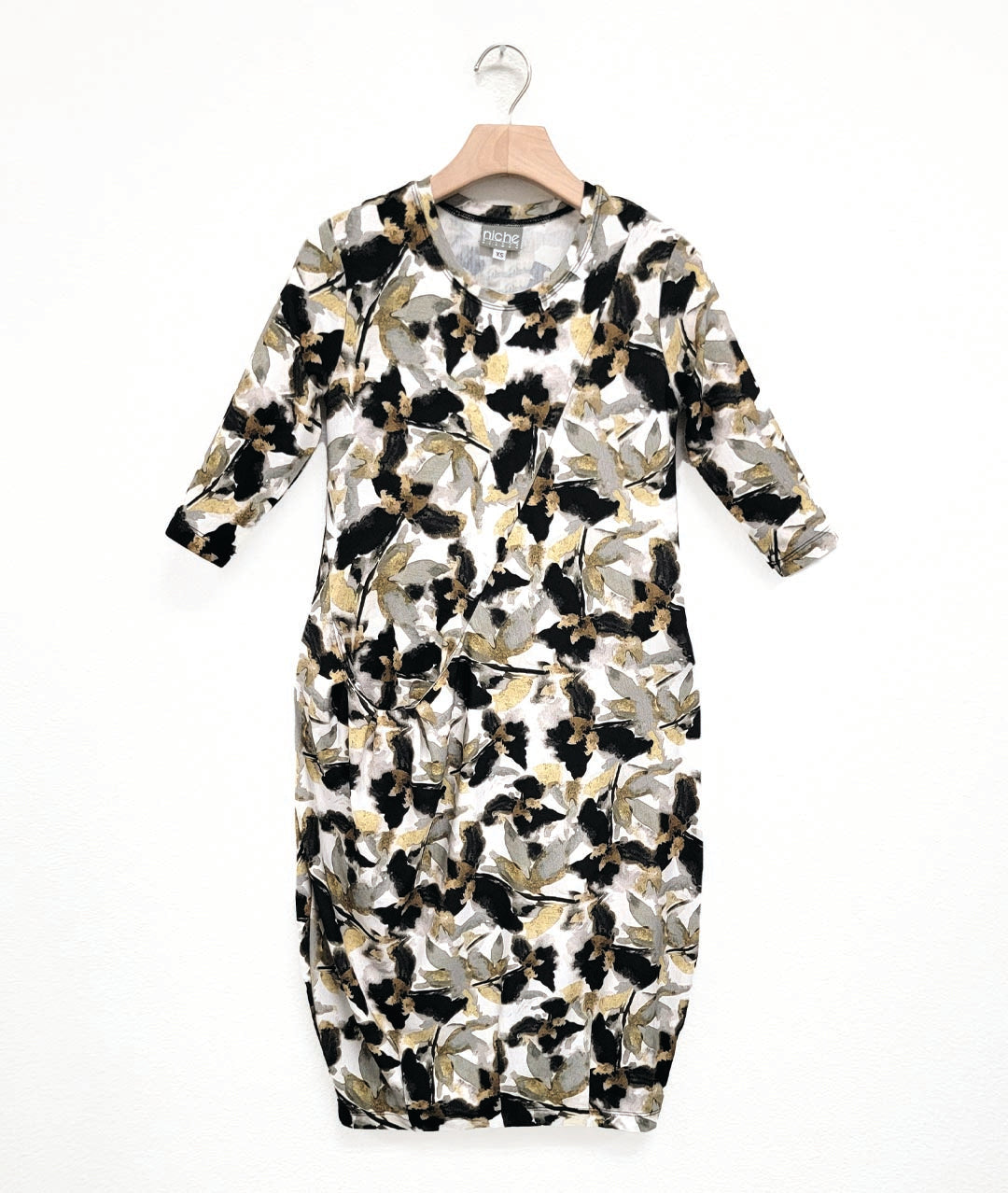 jersey dress with a round neckline, 3/4 sleeves, and an asymmetrical diagonal seam across the body, with a single hip pocket, highlighted by pleats. dress print is a multicolor floral print in black, grey, yellow and white