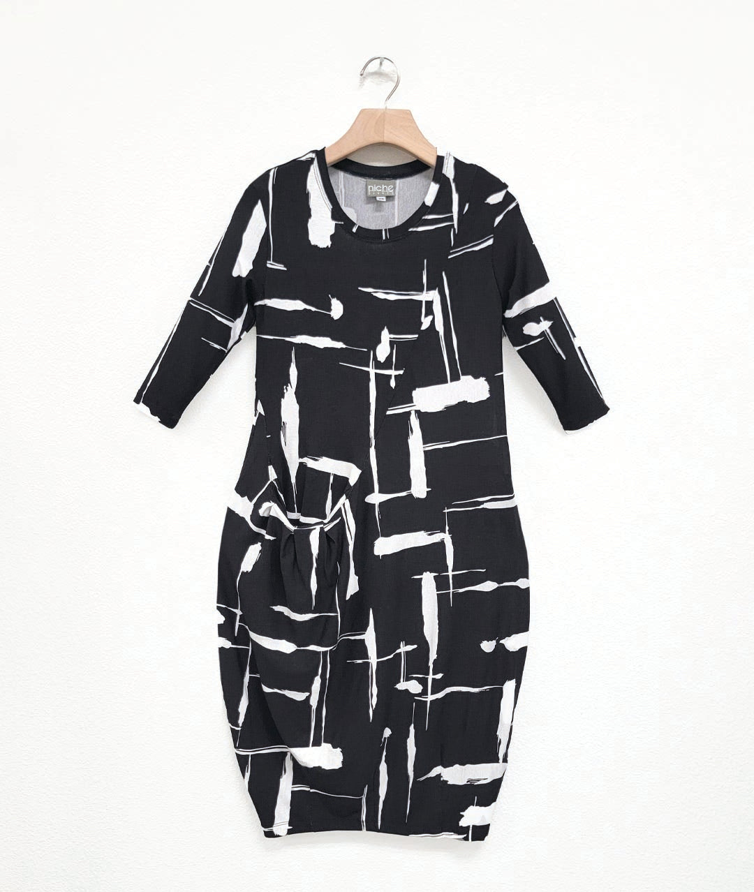 jersey dress with a round neckline, 3/4 sleeves, and an asymmetrical diagonal seam across the body, with a single hip pocket, highlighted by pleats. dress print is black with white brush strokes