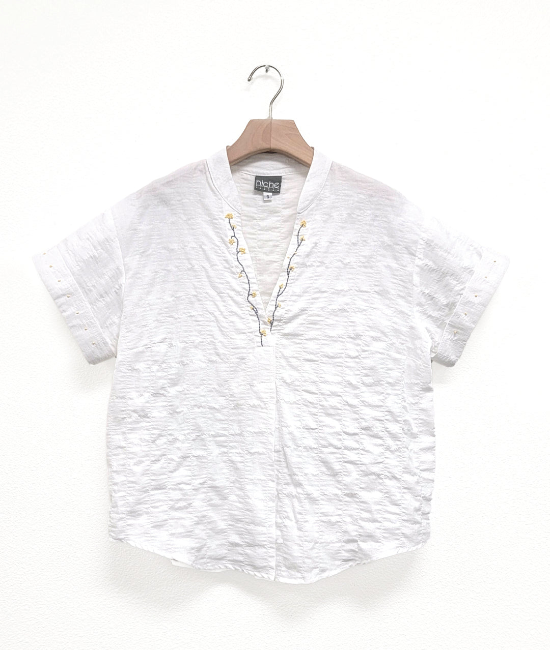 WHITE TEXTURED SHIRT WITH A V-NECK, CUFFED SLEEVES AND A SMALL STANDING COLLAR. floral embroidery at the v-neck, small dots at the sleeve cuffs
