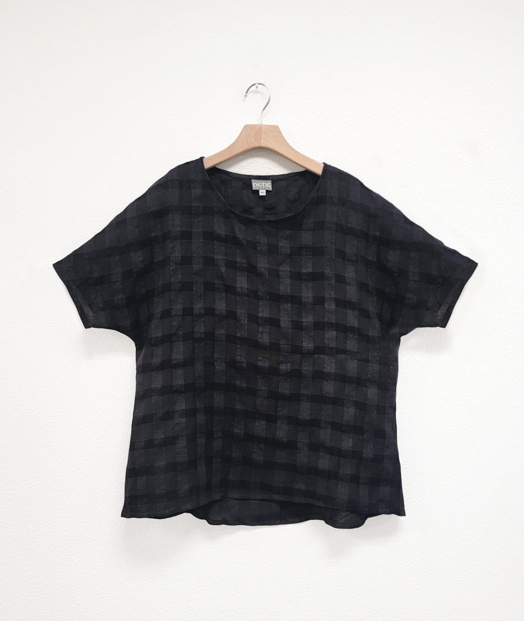 black pullover top with a large rounded neckline, elbow length raglan sleeve, and a large checkered print woven into the fabric