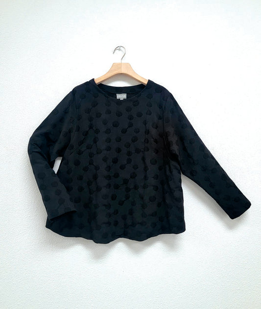 black pullover top with a puckered dot texture. top has a round neckline, long sleeves and a curved hem