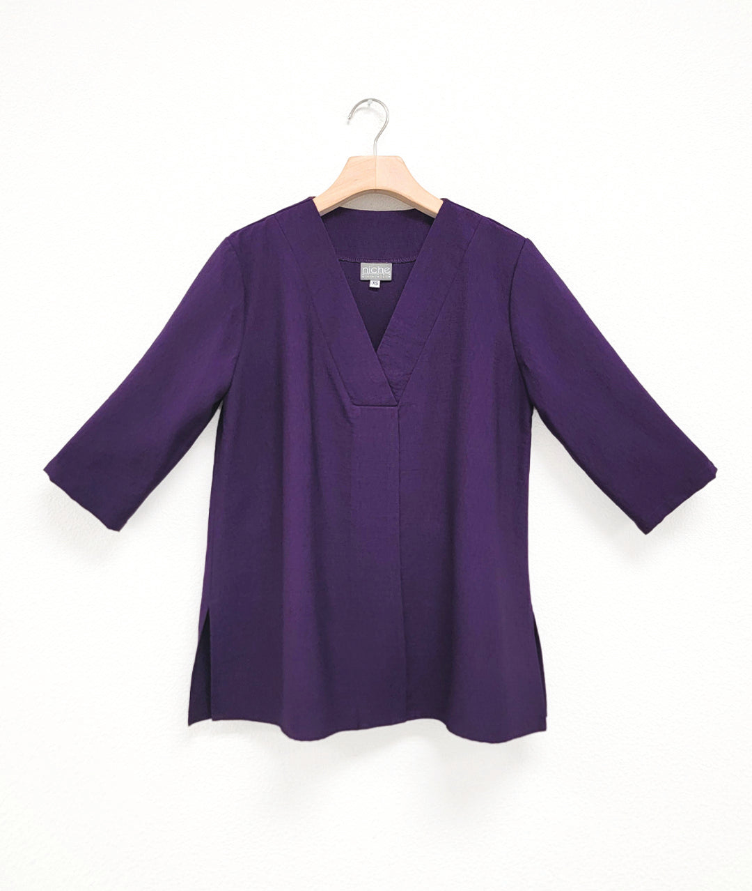 Purple half sleeve top with v-neck on a hanger against a white background