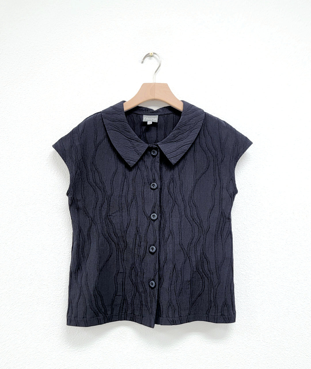 black sleeveless button up shirt with textured pattern on a hanger against a white background