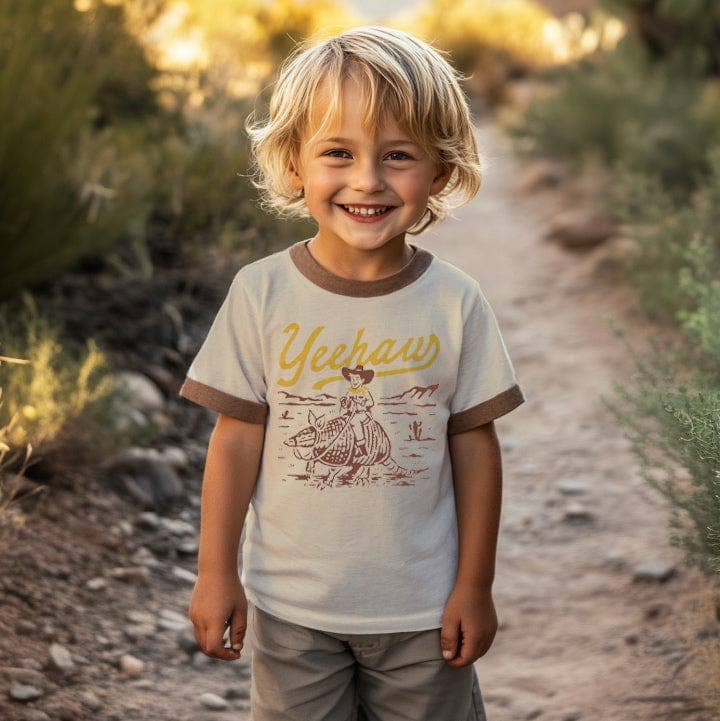 Child wearing a 'Yeehaw' shirt with a cowboy graphic on a dirt path.