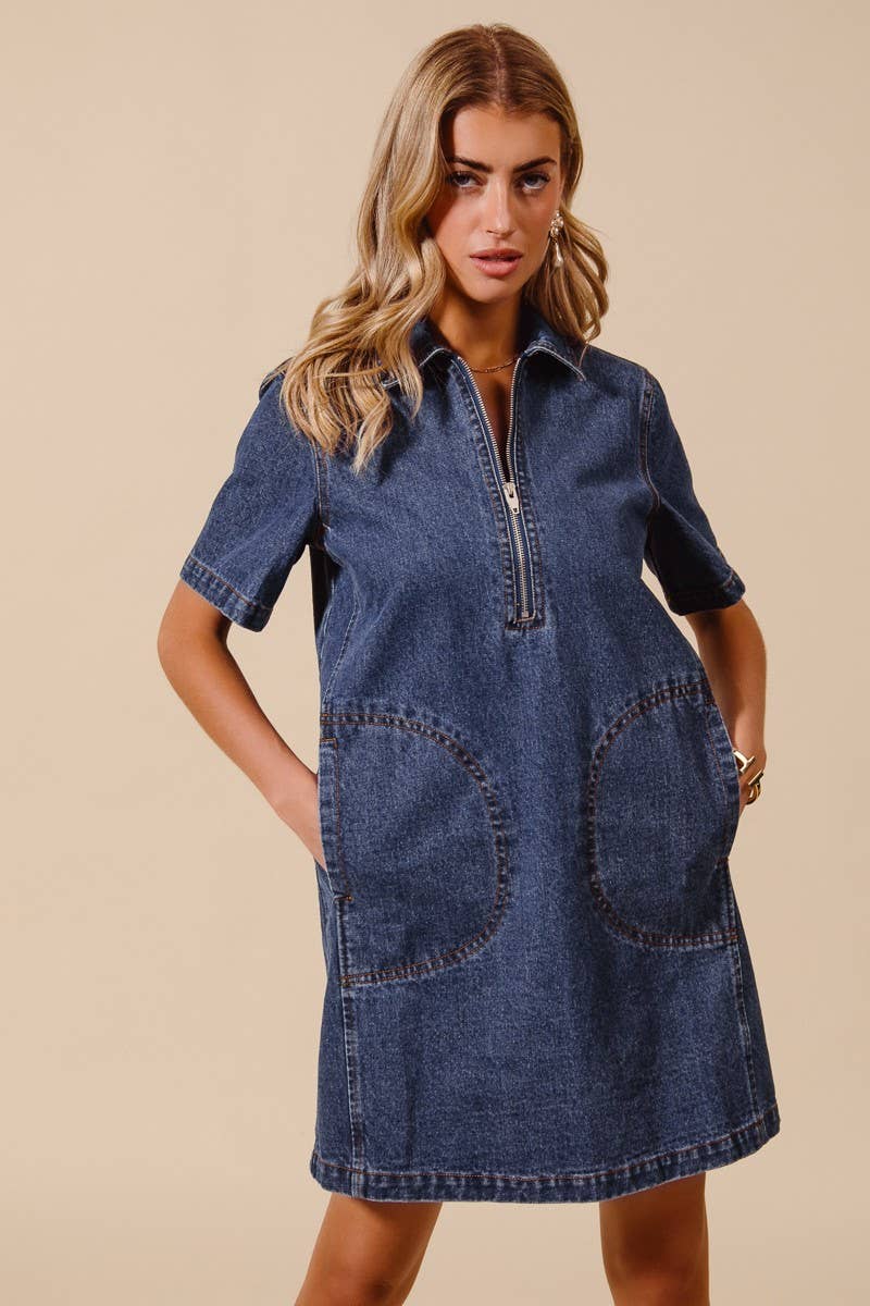 model wearing a denim dress with short sleeves, collar, front zipper and big front sewn pockets on a beige background