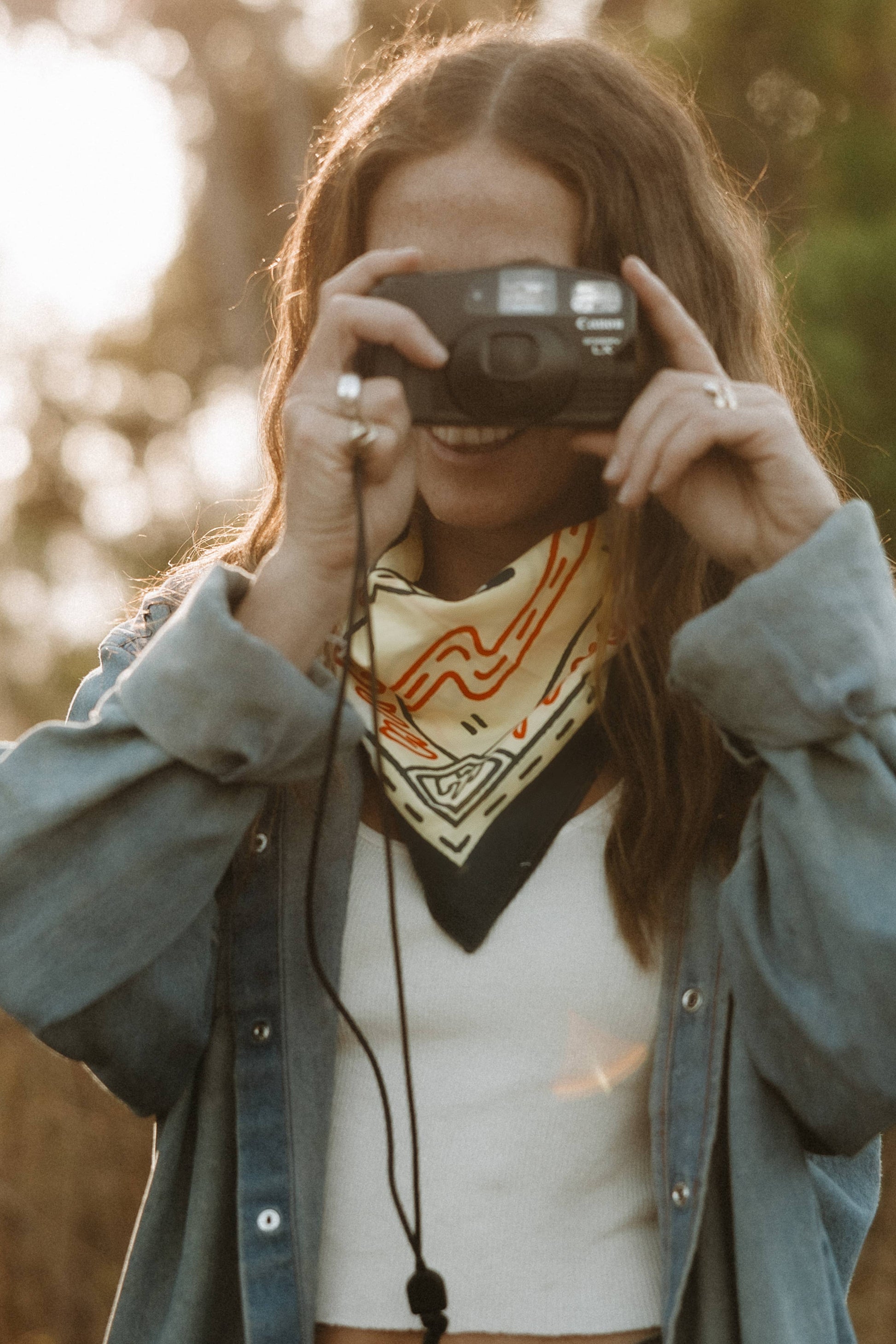 women taking picture with camera wearing bandana around neck, white shirt and jean jacket