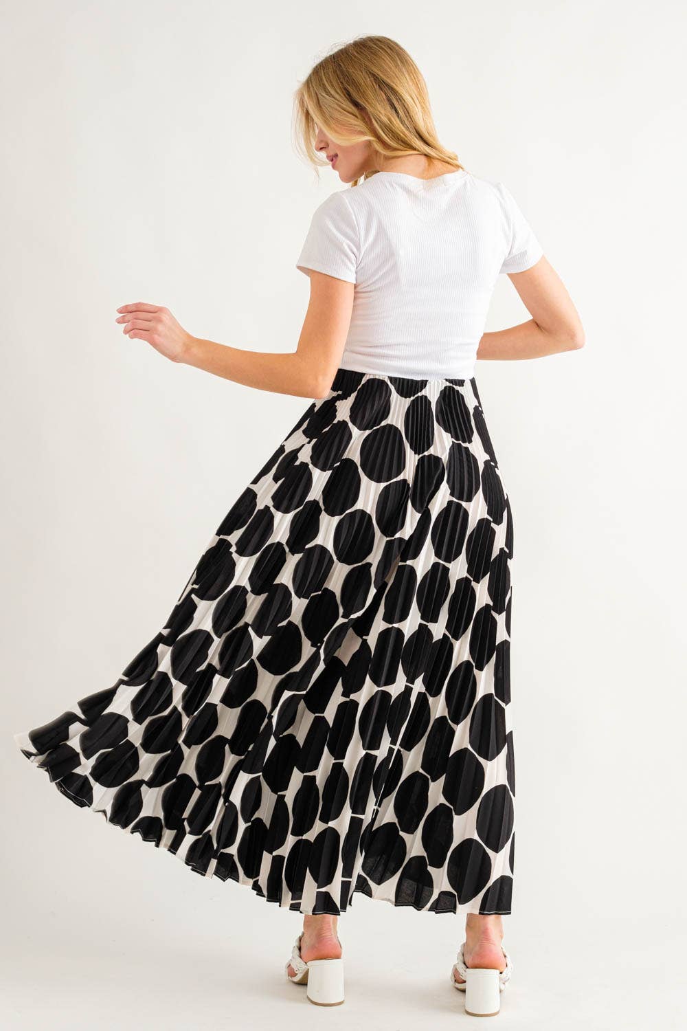 back view of a model wearing a white top and a black polka dot skirt