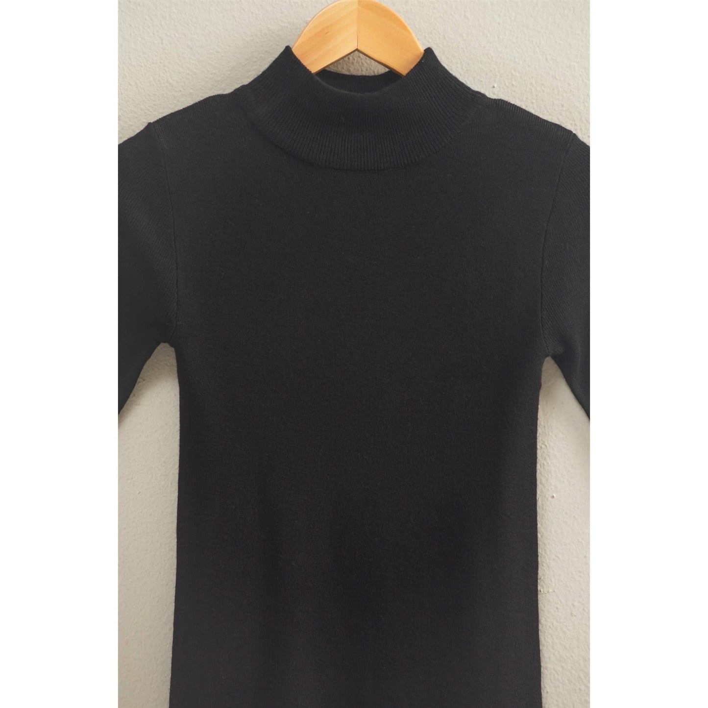 Black mock neck sweater top on a wooden hanger against a neutral background