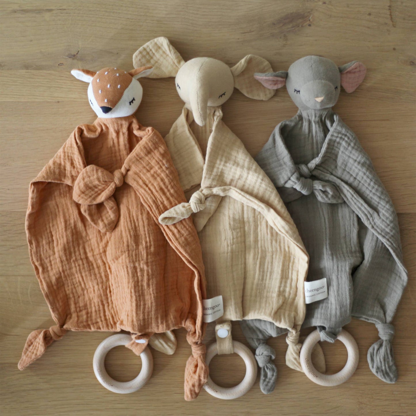 Three baby comfort toys, one resembling a fox, one a mouse, and one a rabbit, on a wooden surface.