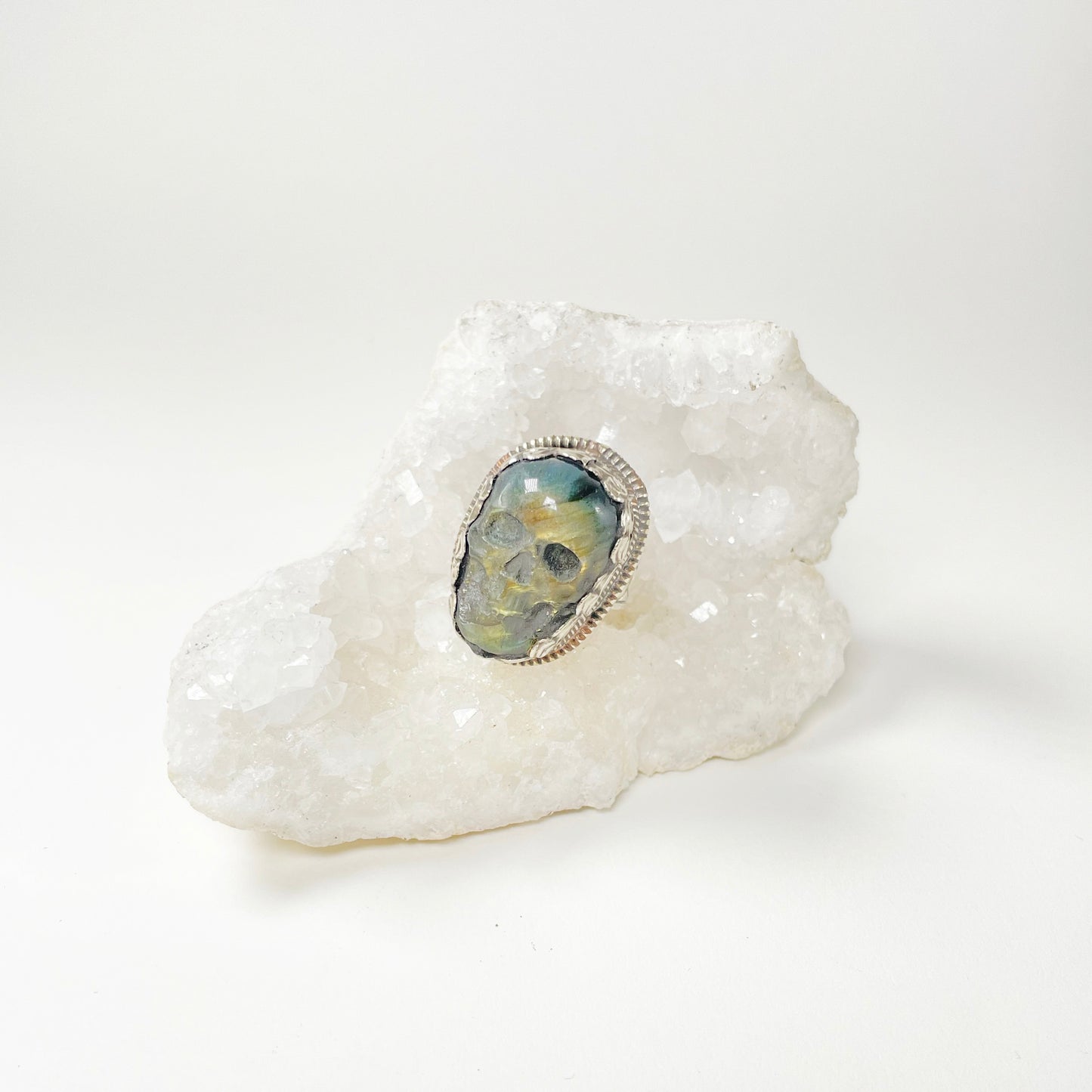 Skull carved Green Labradorite set in detailed Tibetan Silver ring on a white geode crystal.