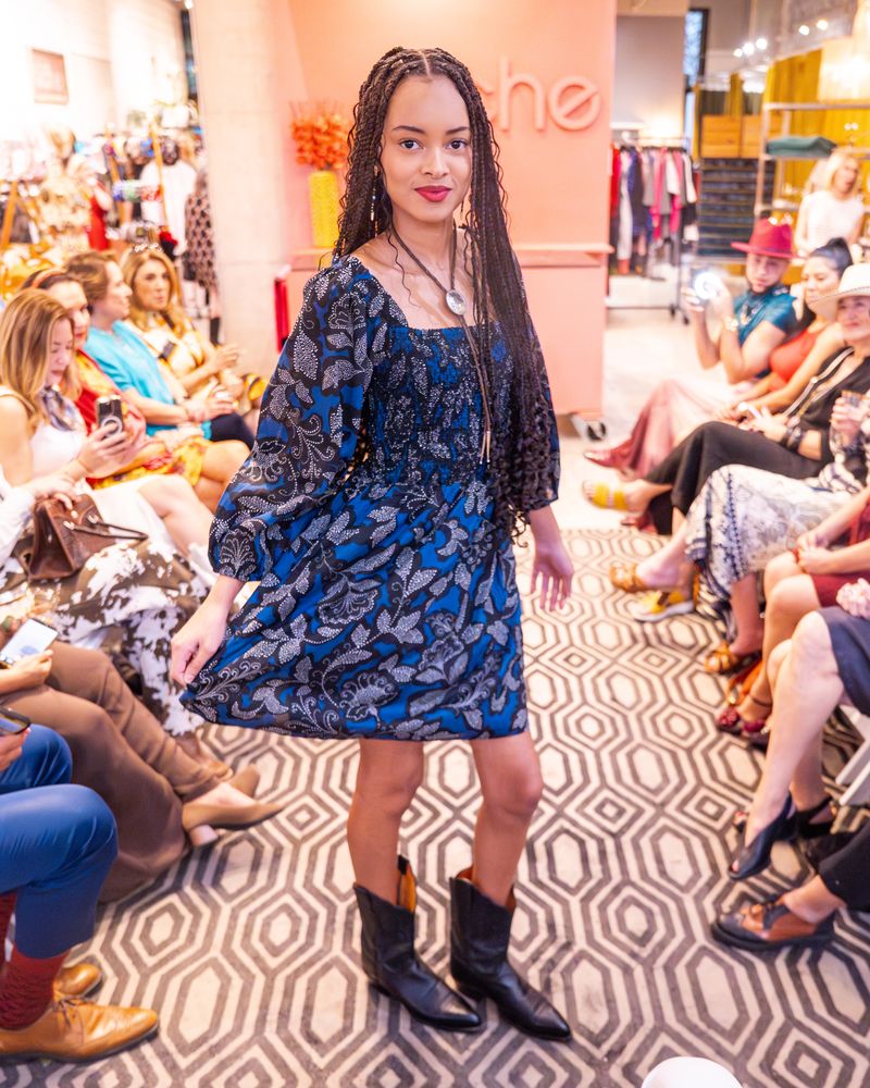model in a blue pattern dress, bolo tie and cowboy boots walking down a runway