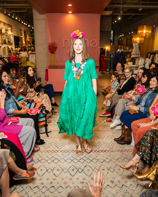 Model in a green dress walking on a runway with an audience watching.