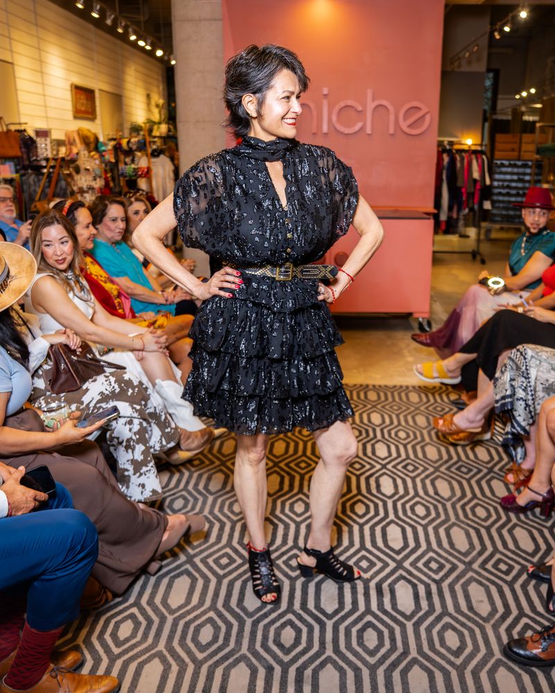 model in a black dress with neck tie and belt walking down runway