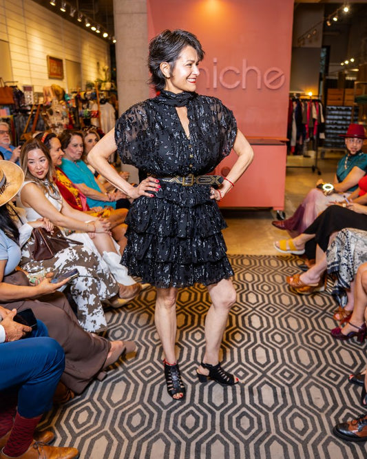 model in a black dress with neck tie and belt walking down runway