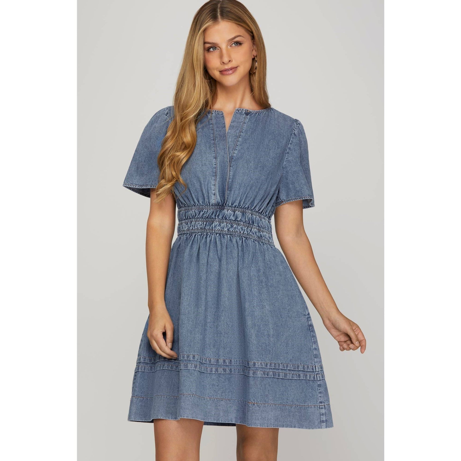 A woman wearing a blue washed denim short sleeve dress with elastic waistband and side pockets