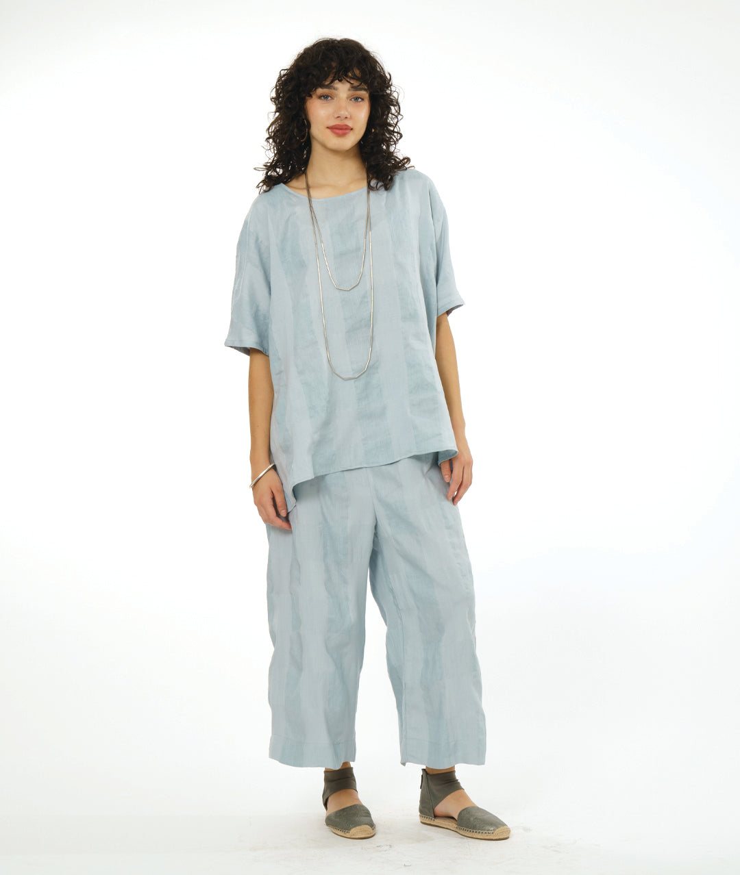 model in a wide leg silver toned pant, with a matching pullover top with a large rounded neckline, elbow length raglan sleeve, and a large checkered print woven into the fabric