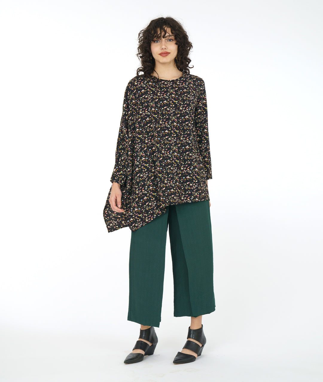 model in a wide leg forrest green pant with a black terrazzo print top. Top is asymmetrical with a drape and cocoon sleeve on one side only