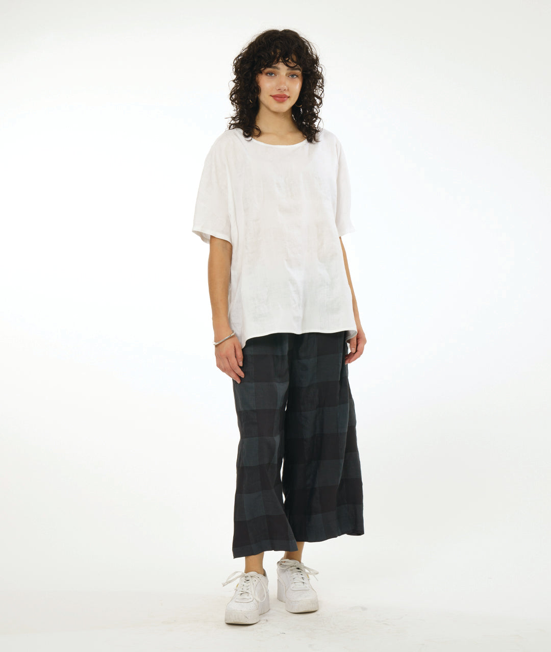 model in a wide leg deep grey pant, white pullover top with a large rounded neckline and an elbow length raglan sleeve. Top and pant both have a large checkered print woven into the fabric