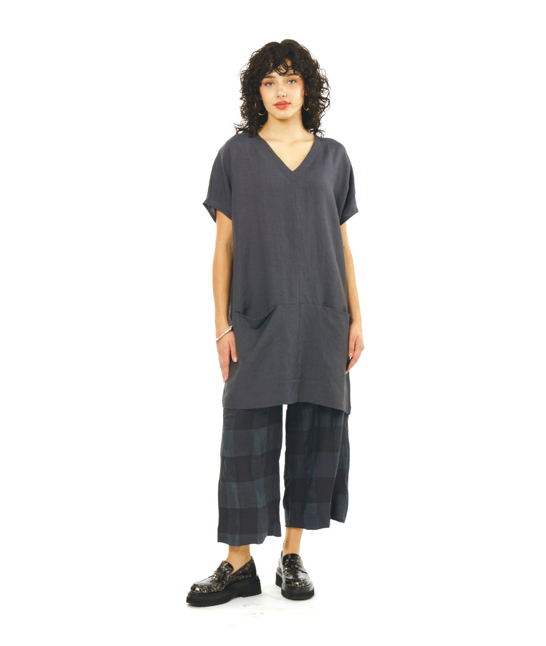 model in a grey pullover dress with a boxy body, capped sleeves a v-neck and pockets set in to a dropped waist seam. worn with a plaid print matching pant