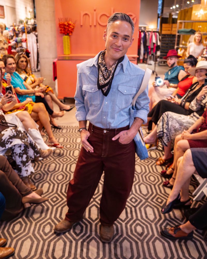 model wearing light blue pearl snap shirt with bandana, burgundy pants and jean tote with rainbow design on a runway
