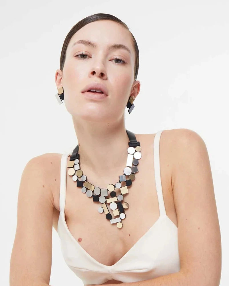 model wearing silver, gold and black geometric shaped necklace and earrings against white background