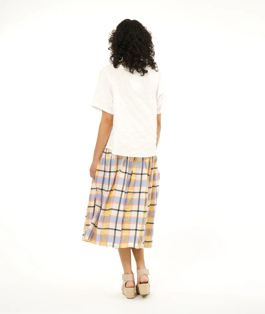 model showing back of full gathered skirt with elastic waist and bias cut yoke in a plaid pastel pattern paired with white tshirt and sandals