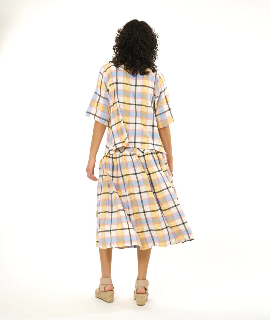 model showing back of boxy and short top with dolman sleeves and a no shoulder seam in a plaid pastel pattern with a matching midi skirt and sandals