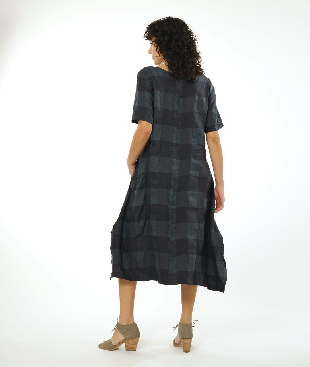 model in a large check print dress with an asymmetrical body, round neckline, elbow length sleeves, and contrasting panels across the body