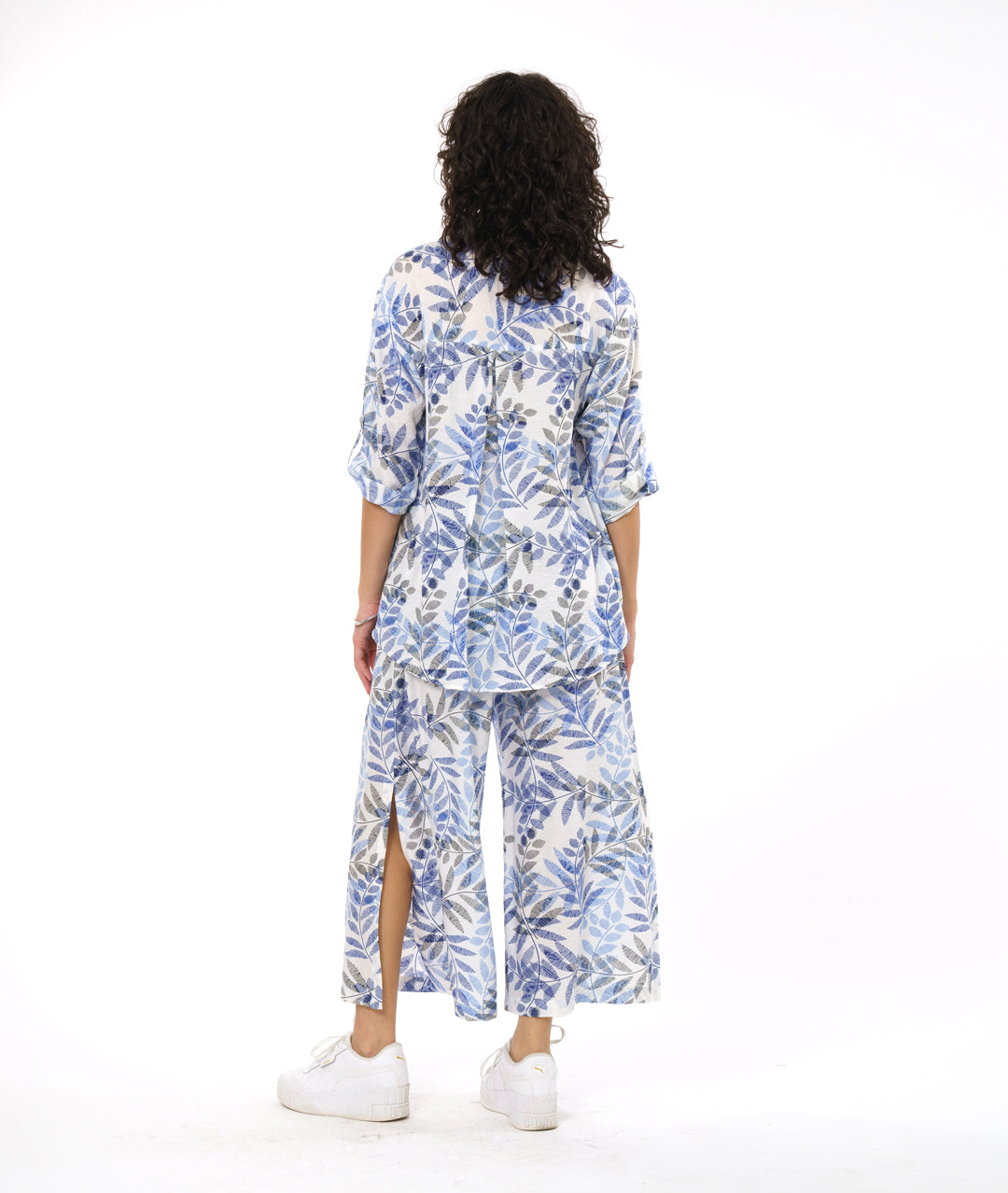 model in a wide leg white pant with a blue and black leaf print. worn with a button down blouse with rolled sleeves in the same fabric