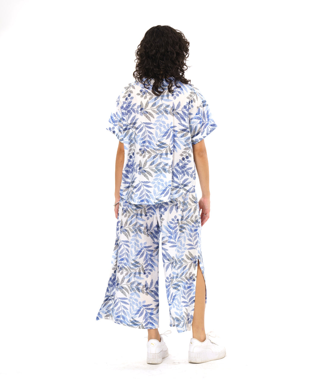 model in a white boxy pullover with a blue and black leaf print. worn with a matching wide leg pant with a slit up either side