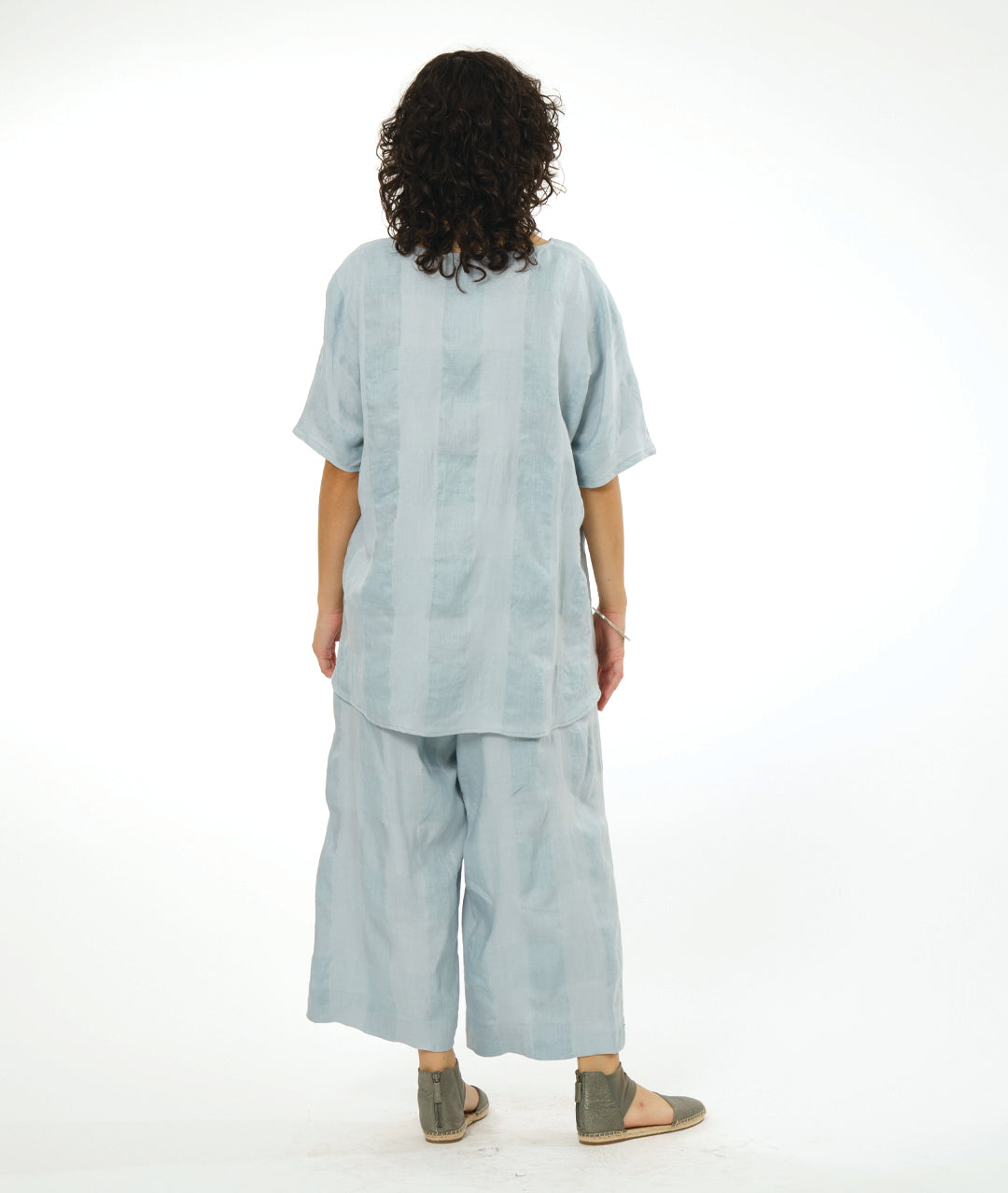 model in a wide leg silver toned pant, with a matching pullover top with a large rounded neckline, elbow length raglan sleeve, and a large checkered print woven into the fabric