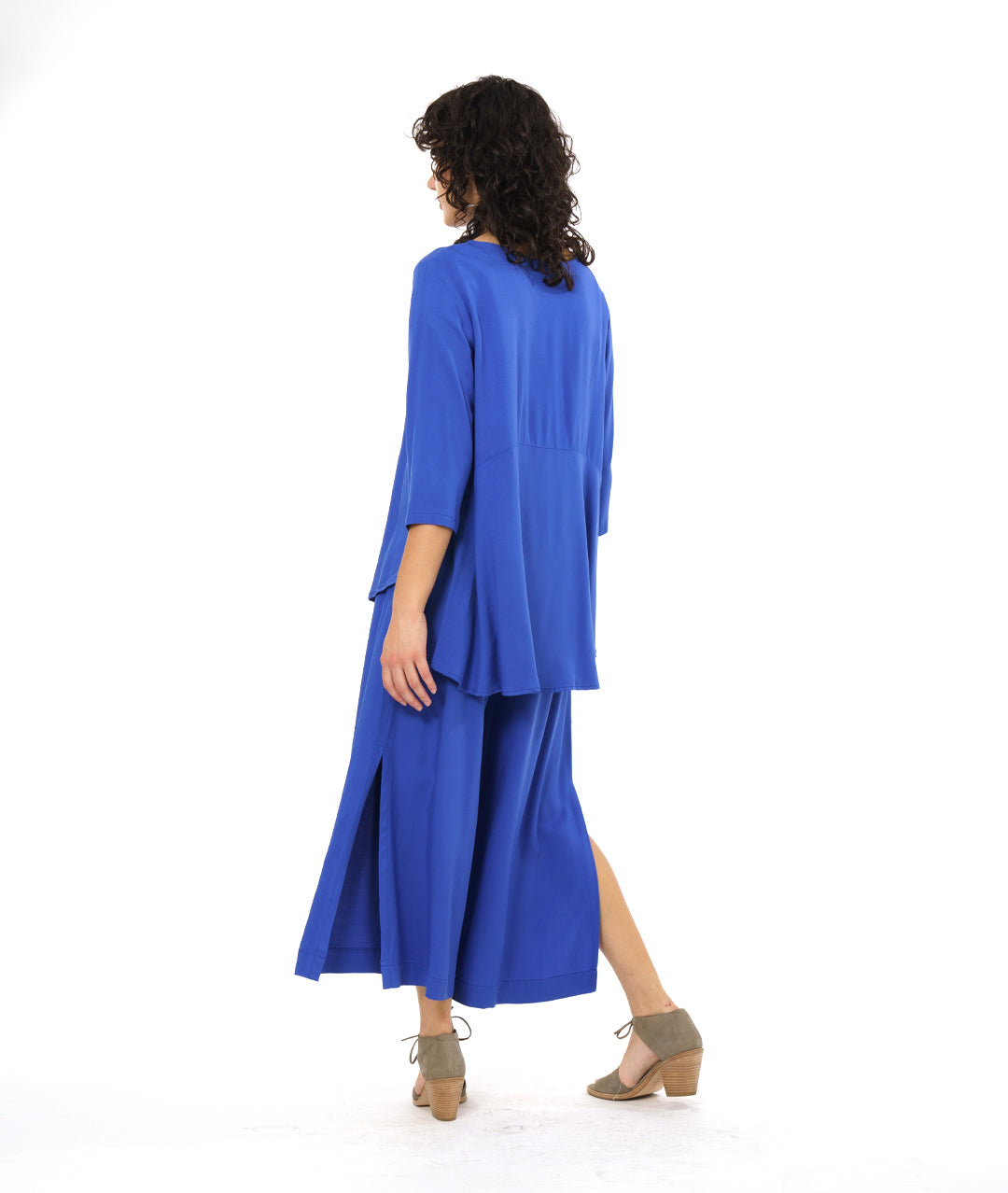 model in a wide leg periwinkle pant with a side slit on either side, worn with a matching pullover top with 3/4 sleeves and a rounded hem, dipping lower in the back