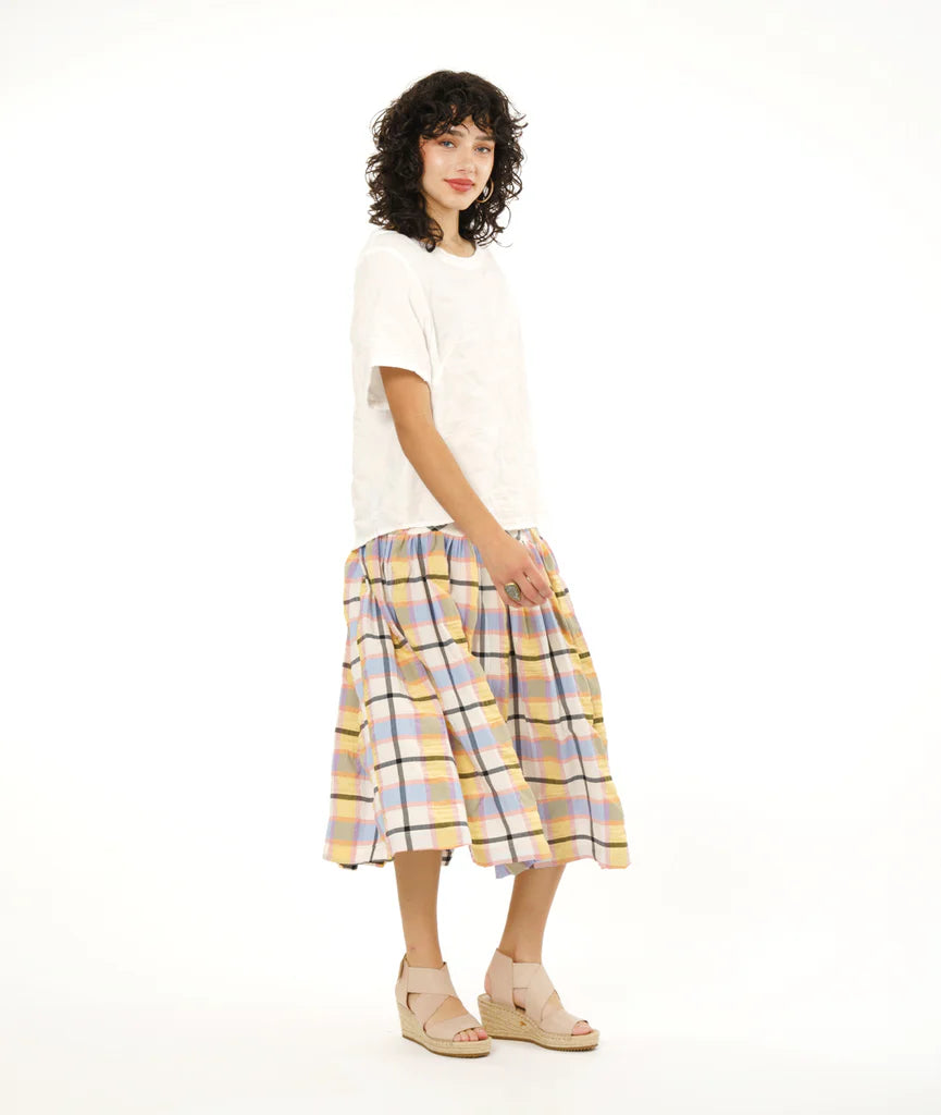 model wearing full gathered skirt with elastic waist and bias cut yoke in a plaid pastel pattern paired with white tshirt and sandals