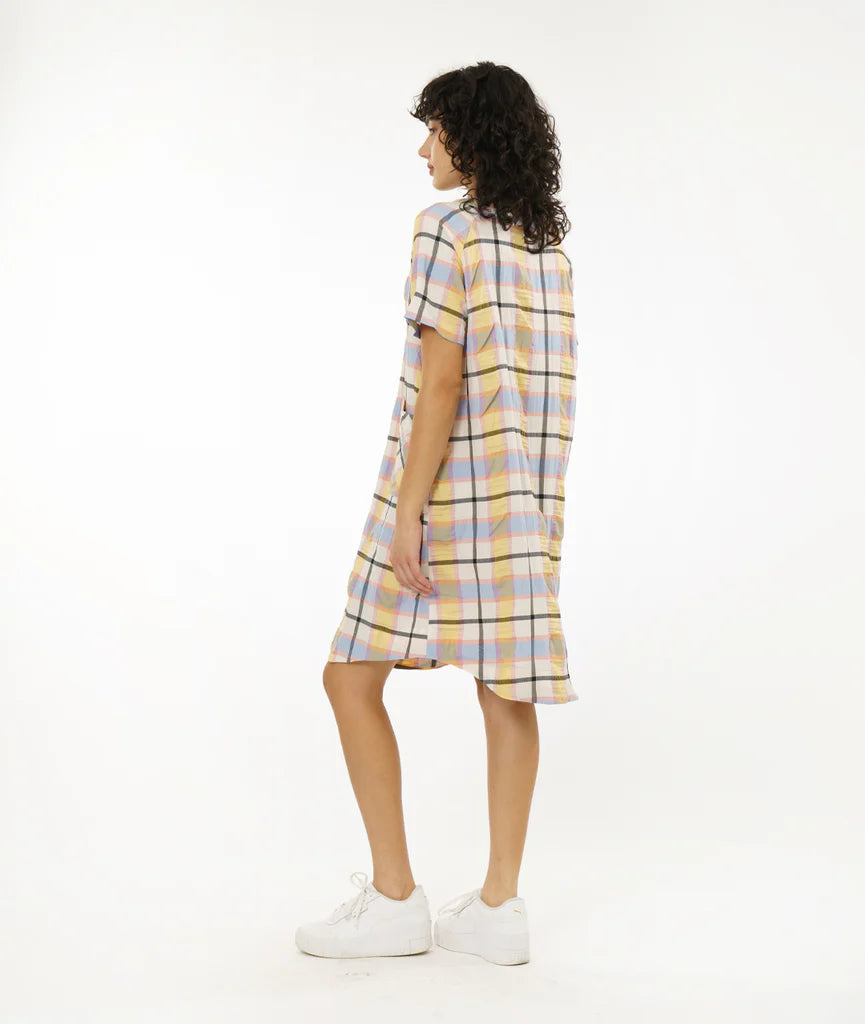 model wearing round hem dress that hits below the knee with patch pockets, short sleeves and boat neck collar in a plaid pastel pattern paired with white sneakers