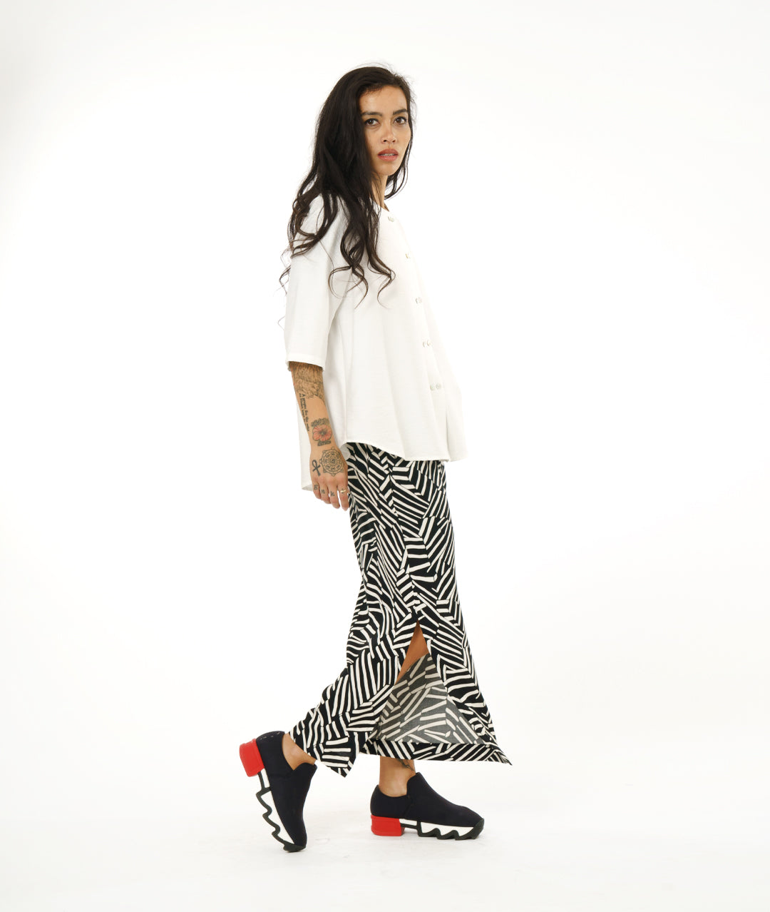model in a black and white broken stripe print pant with a long slit at the side seams, worn with a collar less white button down blouse with 3/4 sleeves