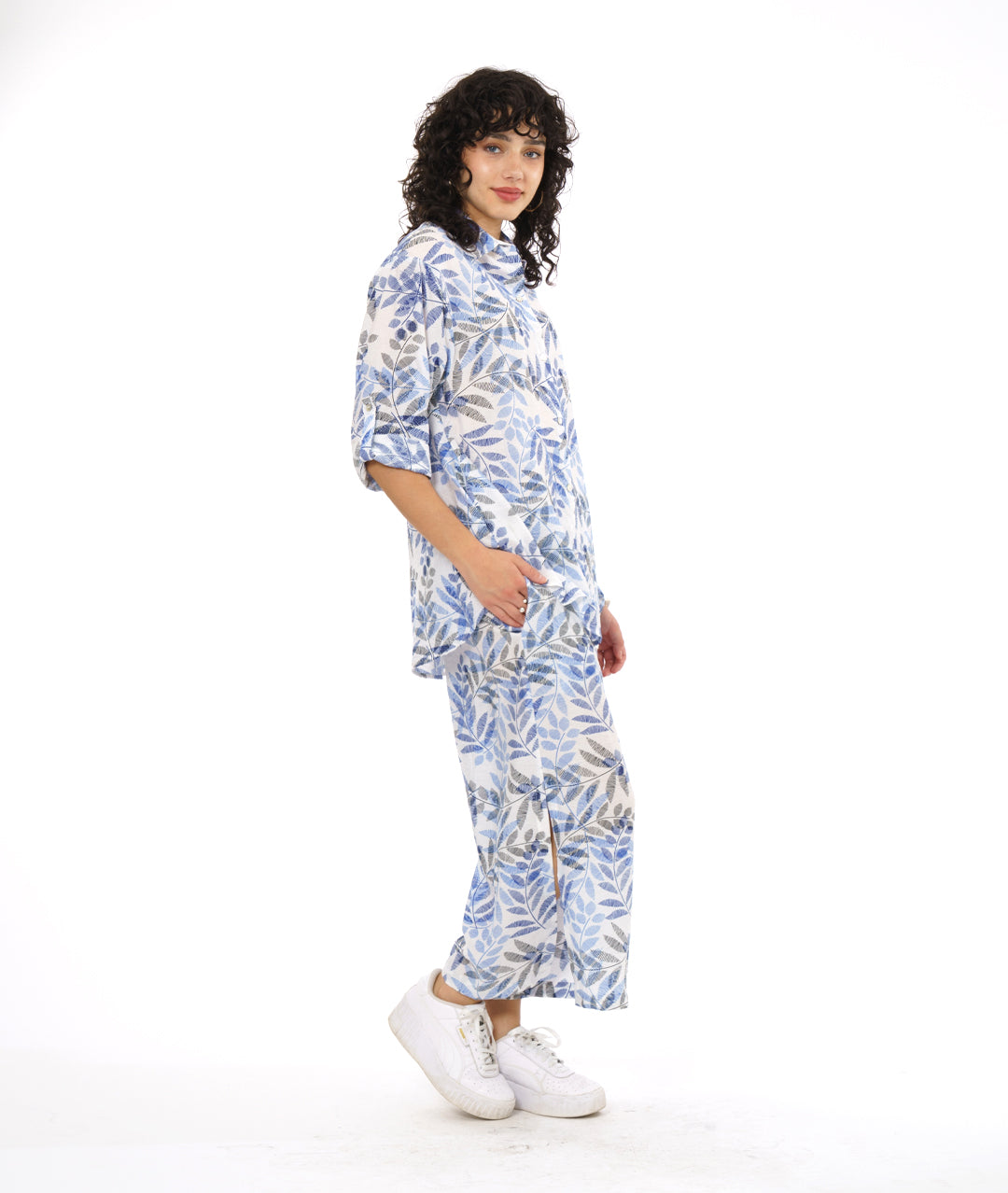 model in a wide leg white pant with a blue and black leaf print. worn with a button down blouse with rolled sleeves in the same fabric
