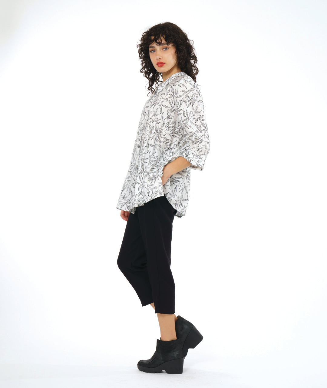 model in a slim black cropped pant, worn with a white button down blouse with a twinbutton detail, 3/4 sleeves, a long body and a floral print