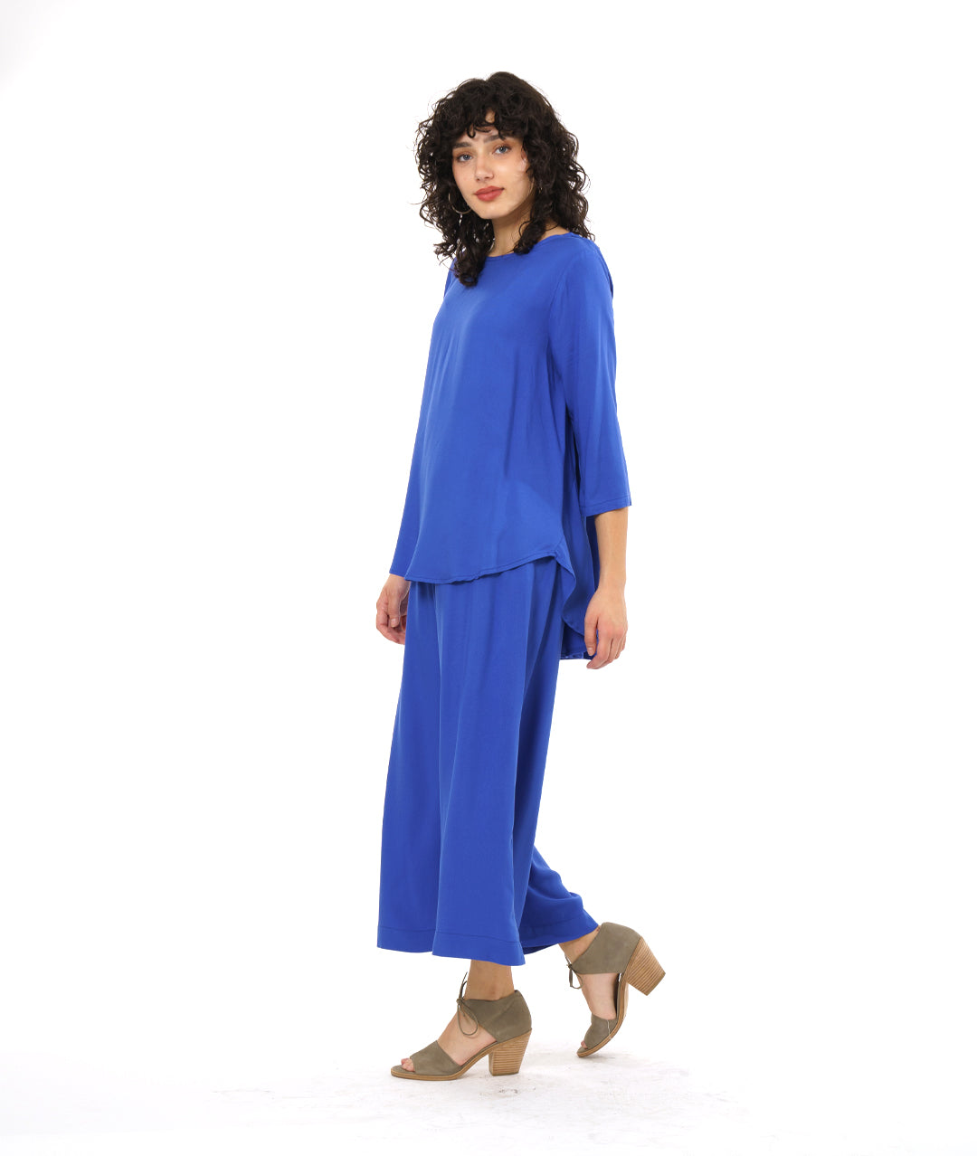 model in a wide leg periwinkle pant with a side slit on either side, worn with a matching pullover top with 3/4 sleeves and a rounded hem, dipping lower in the back